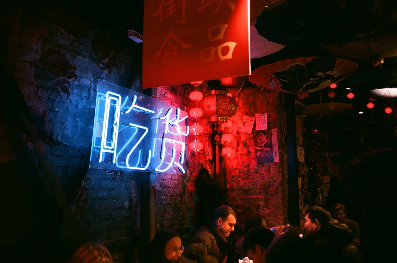 A crowded bar with brick walls, red lanterns and a blue neon sign